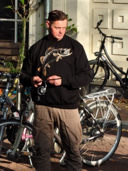 Mężczyzna łowiący ryby w Amsterdamie, prezentuje czarną bluzę wędkarską z nadrukiem sandacza