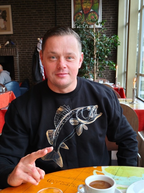 Mężczyzna siedzący w kawiarni prezętuje bluze z nadrukiem sandacza od marki EXOART